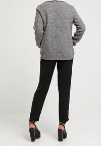 Grå tröja med en texturerad yta och vit krage, kombinerad med svarta tapered byxor och kraftiga svarta klackskor.