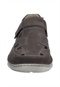 Scarpa in suede marrone con motivi intagliati, cinturino regolabile e cuciture beige lungo il bordo. Suola in gomma con dettagli testurizzati.