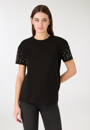 T-shirt nera in cotone con maniche corte, decorata con borchie argentate sulle spalle. Tessuto liscio, vestibilità comoda e scollatura rotonda.