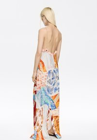 Multikleurige maxi-jurk met een diepe V-back, voorzien van bloem- en abstracte patronen, dunne bandjes en een vloeiende textuur van de stof.