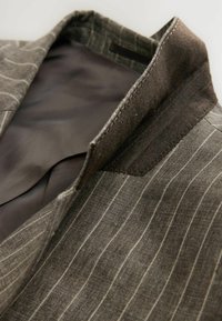 Brown striped blazer with a textured collar and smooth inner lining. The fabric features thin white lines and a structured design.