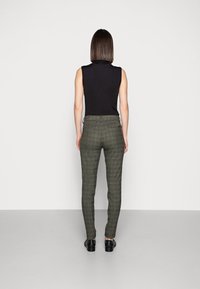 Top negro ajustado sin mangas combinado con pantalones de cuadros verdes a medida, mostrando una silueta esbelta y una textura sutil en la parte posterior.