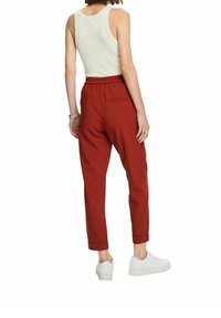 Spodnie w kolorze rdzy, z elastycznym pasem, zwężane nogawki i podwinięte mankiety, zestawione z dopasowanym kremowym topem na ramiączkach i białymi trampkami.