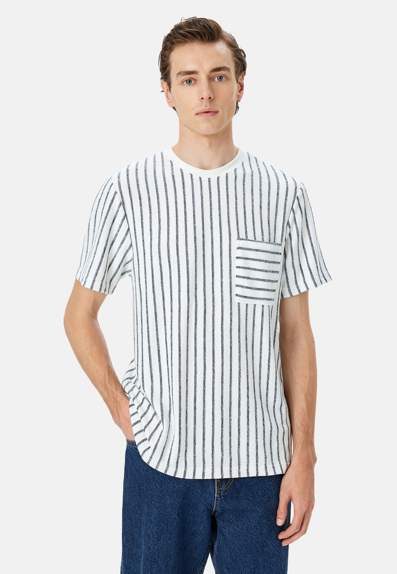 Camiseta de manga corta a rayas en blanco y azul marino, con cuello redondo, un bolsillo en el pecho izquierdo y un corte relajado. Tejido suave con líneas verticales.