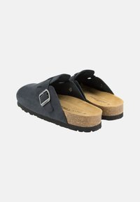 Schwarze Wildlederschuhe mit einem Korkfußbett, ausgestattet mit einer seitlichen Schnalle und einem offenen Rückendesign, strukturiertem Sohlendesign und glatter Oberflächenstruktur.