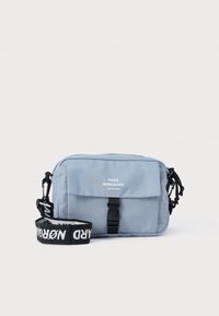 Jasnoniebieska torba na ramię wykonana z trwałego materiału, wyróżniająca się przednią klapą, czarnymi elementami metalowymi oraz nadrukowanym regulowanym paskiem.