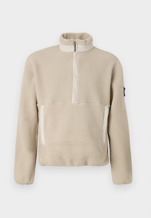 Sudadera de forro polar beige con cuello alto, cierre de cremallera de cuarto en la parte delantera y dos bolsillos frontales. Tejido texturizado con acentos beige contrastantes.