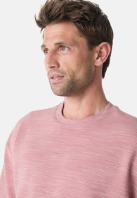 Sudadera de cuello redondo rosa claro que presenta un tejido texturizado con sutiles rayas horizontales y un ajuste relajado. Detalle de escote suave.