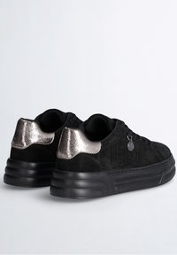 Black suede sneakers with metallic silver accents on the heel, round toe, black textured sole, and branded detailing on the side.
