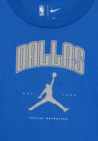 Mėlynas medvilnės marškinėliai su pilku tekstu "DALLAS", Jordan silueto logotipu ir "DALLAS MAVERICKS" su "EST. 1980" žemiau.