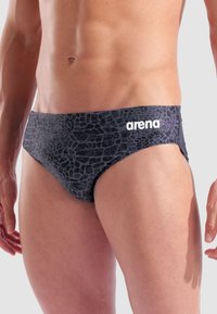 Sorte svømmebukser med et tekstureret krokodillemønster, udstyret med et hvidt "arena" logo på venstre hofte. Klassisk snitdesign og glat stof.