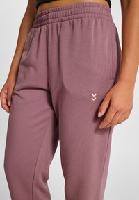 Helle mauvefarbene Jogginghosen mit elastischem Bund, Seitentaschen und einem kleinen bestickten Chevron-Detail in Creme auf dem unteren Bein.