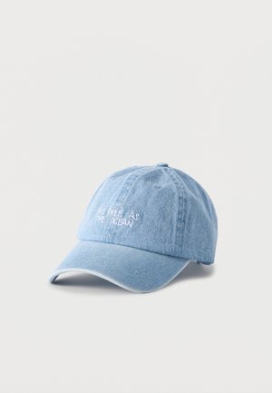 Casquette de baseball en denim bleu clair avec texte brodé blanc « AS FREE AS THE OCEAN » à l'avant, présentée sur un fond blanc uni.