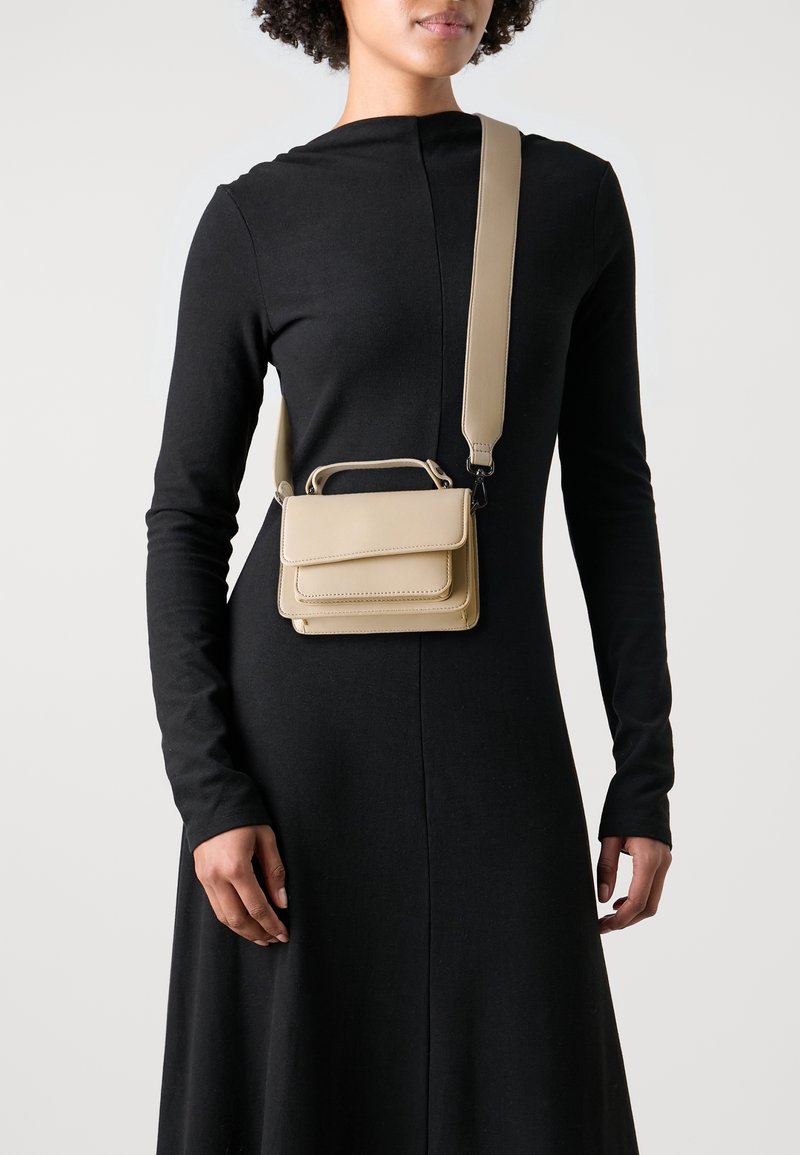 Borsa a tracolla in pelle beige con design strutturato, dotata di manico superiore e tracolla removibile. Texture liscia, accenti minimalisti.