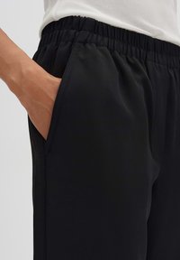 Zwarte joggingsbroek van gladde stof, met een elastische tailleband en een zijzak. Strak ontwerp met subtiele stikdetails.