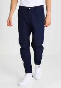 Marineblauwe, taps toelopende joggerbroek van zachte stof, met een elastische tailleband, trekkoord en zijzakken. G gedragen met witte sneakers.