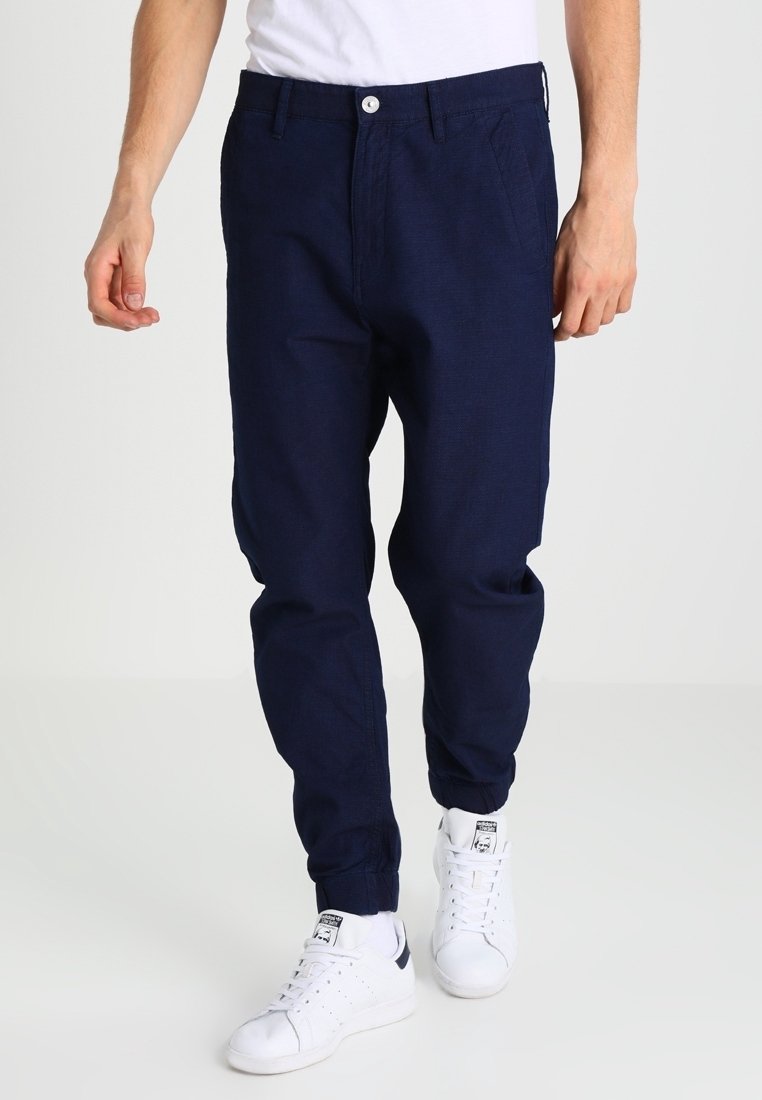 Marineblauwe, taps toelopende joggerbroek van zachte stof, met een elastische tailleband, trekkoord en zijzakken. G gedragen met witte sneakers.