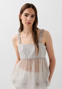 Top grigio chiaro con spalline a volant, design stratificato e tessuto inferiore trasparente. Morbido al tatto e vestibilità rilassata, adatto per un abbigliamento informale.
