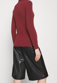 Bordeaux ribbed coltrui gecombineerd met zwarte glanzende geplooide culottes, die een gestructureerde stof en een relaxte pasvorm benadrukken.