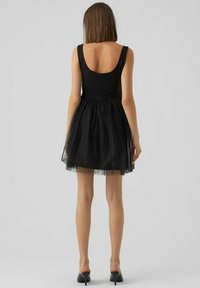 Schwarzes Kleid mit figurbetontem Oberteil und Tüllrock. Verfügt über einen runden Rückenausschnitt, ärmelloses Design und wird mit schwarzen High Heels kombiniert.