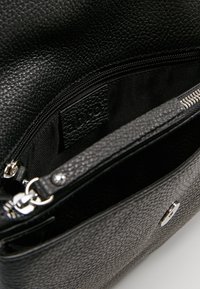 Czarna torebka ze strukturalnej skóry z zamkiem błyskawicznym, z gładką podszewką, srebrnymi akcentami i wytłoczonym logiem marki.
