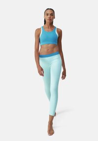 Un reggiseno sportivo in una gradazione di tonalità blu, abbinato a leggings azzurri chiari con vita elastica; tessuto liscio e elasticizzato.