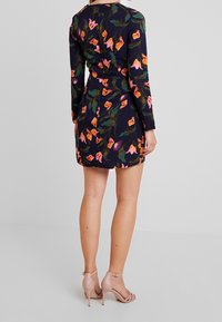 Sukienka w kwiatowy wzór w granatowym kolorze z różowymi i zielonymi akcentami. Długie rękawy, dopasowany fason w talii i krótki dół. Noszona z cielistymi sandałami na wysokim obcasie.