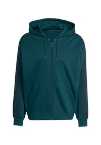 Τζάκετ φούτερ σε τζακίνη απόχρωση, κατασκευασμένο από μαλακό υλικό, διαθέτοντας καγκουρό τσέπη, κουκούλα με κορδόνι και σκούρες κόκκινες ρίγες στα πλάγια με λογότυπο στο στήθος.