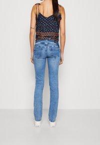 Blue denim jeans with a slight flare and fading, paired with a navy patterned crop top featuring thin straps and tassel accents.