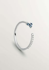 Pulsera de plata con un acabado suave, con gemas azules y una fila de piedras transparentes a lo largo de un borde. Diseño minimalista y forma abierta.