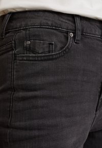 Zwarte denim jeans met een vijf-pocket ontwerp, zichtbare stiksels en een kleine klinknagelaccent op de voorkzak. Soepele textuur.