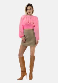 Zijdeachtige lange mouw crop top in het roze met een geplooide textuur, gecombineerd met een beige hoge taille minirok en bruine stiletto laarzen tot de knie.