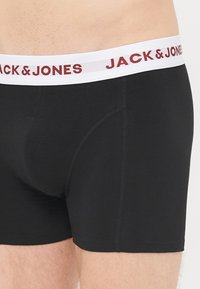 Schwarze Baumwollboxershorts mit einem weißen Bund, der "JACK & JONES" in Burgunderrot zeigt. Glatte Textur, enganliegende Passform und geschwungenes Pouch-Design.