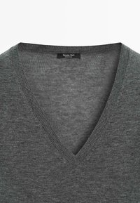 Szary sweter z dekoltem w serek wykonany z cienkiej dzianiny z prążkowanymi wykończeniami. Metka z napisem "Massimo Dutti", czysty design i gładka faktura.