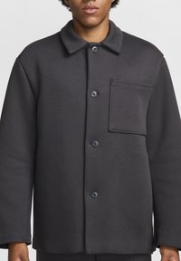 Ciemnoszara, oversizeowa kurtka na guziki wykonana z miękkiego materiału, z kołnierzykiem, kieszenią z przodu i czterema guzikami z przodu.