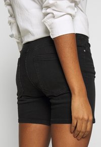 Pantalones cortos de mezclilla negra con un diseño ajustado, cintura de altura media y dos bolsillos traseros. La tela tiene una ligera elasticidad y una textura suave.