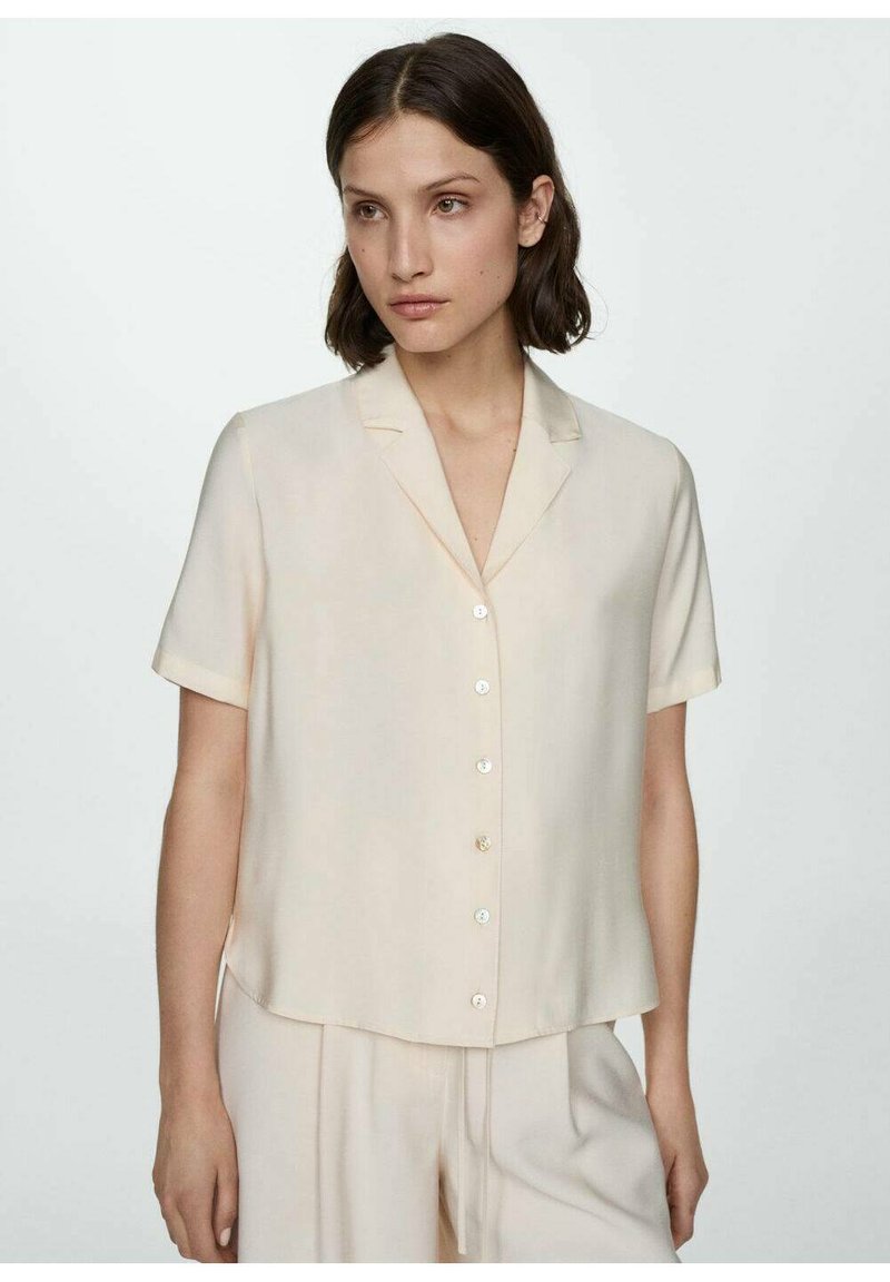 Blusa a maniche corte di colore beige chiaro in un tessuto setoso, con scollatura a V e piccoli bottoni davanti, caratterizzata da una vestibilità comoda e colletto.