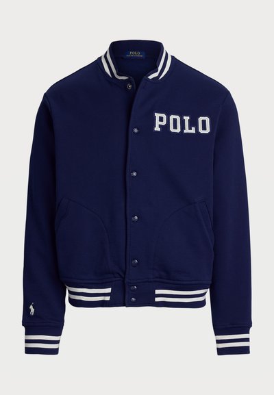 Mørkeblå varsity-jakke med hvite ribbede mansjetter og midjebånd, med broderte "POLO" bokstaver og to frontlommer.