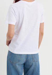 Camiseta blanca de algodón con mangas cortas y cuello redondo, combinada con jeans de mezclilla azul que tienen dos bolsillos traseros.