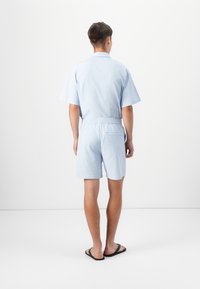 Hellblaues kurzärmeliges Hemd und passende Shorts aus leichtem Stoff. Gummibund an den Shorts, legeres Design und Detail mit Gesäßtasche.