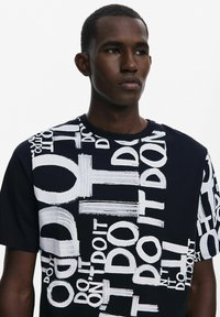 Camiseta negra de manga corta con texto blanco en diferentes tamaños y orientaciones, con una textura suave y cuello redondo.