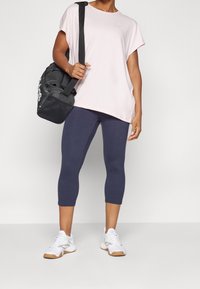 Luźna, jasnoróżowa koszulka z krótkim rękawem, granatowe legginsy 3/4 oraz białe sneakersy z jasnoszarymi detalami. Czarna torba sportowa z logo.