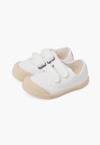 Des chaussures en toile blanches avec une semelle en caoutchouc beige, présentant deux brides Velcro, un bout arrondi et de simples détails de couture sur les côtés.