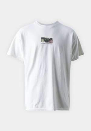 Wit katoenen T-shirt met een vierkante afbeelding met groene bladeren en bloemen, en de tekst "STEP INTO SERENITY" onder het ontwerp.