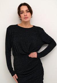 Schwarzes Strickkleid mit langen Ärmeln, das eine geraffte Taille, texturierten Stoff und subtile metallische Fäden aufweist. Glatte Oberfläche.