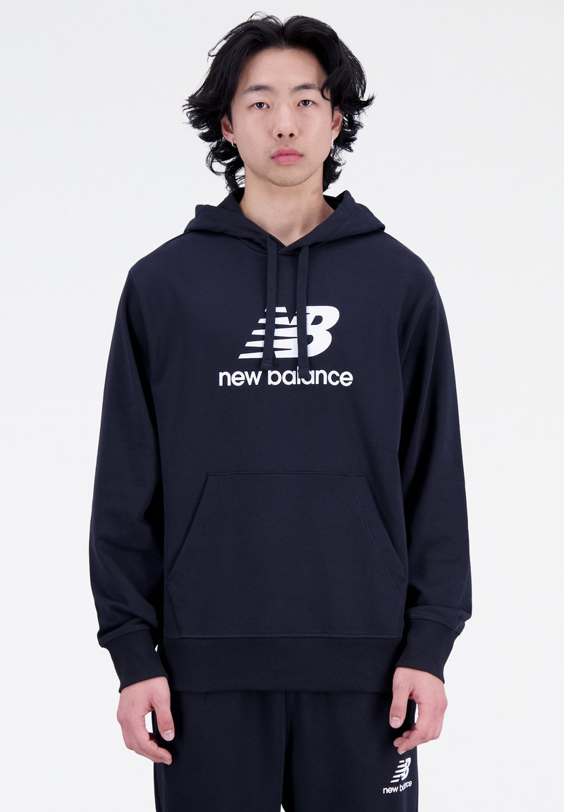 Sudadera de algodón azul marino con un bolsillo frontal, logo blanco de "New Balance" y cordones. Presenta un corte relajado y puños acanalados.
