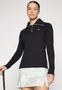 Black ribbed long-sleeve top with a white-lined polo collar, featuring a three-button placket and a logo on the chest.