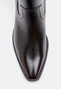 Črni usnjeni gležnjar z ostro konico, gladkim zaključkom in dekorativnim šivanjem ob robovih. Ravna gumijasta podplat, minimalističen dizajn.