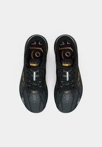 Tênis atléticos pretos com um cabedal em malha texturizada, apresentando detalhes amarelos, elementos refletivos e atacadores pretos. Projetados para desempenho.