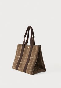 Καφέ καρό τσάντα tote με σκούρες καφέ λαβές, ορθογώνιο σχήμα και ένα μικρό στρογγυλό χρυσό έμβλημα κοντά στο κέντρο της κορυφής.